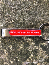 Load image into Gallery viewer, keychain with bottle opener Remove Before flight written in white.